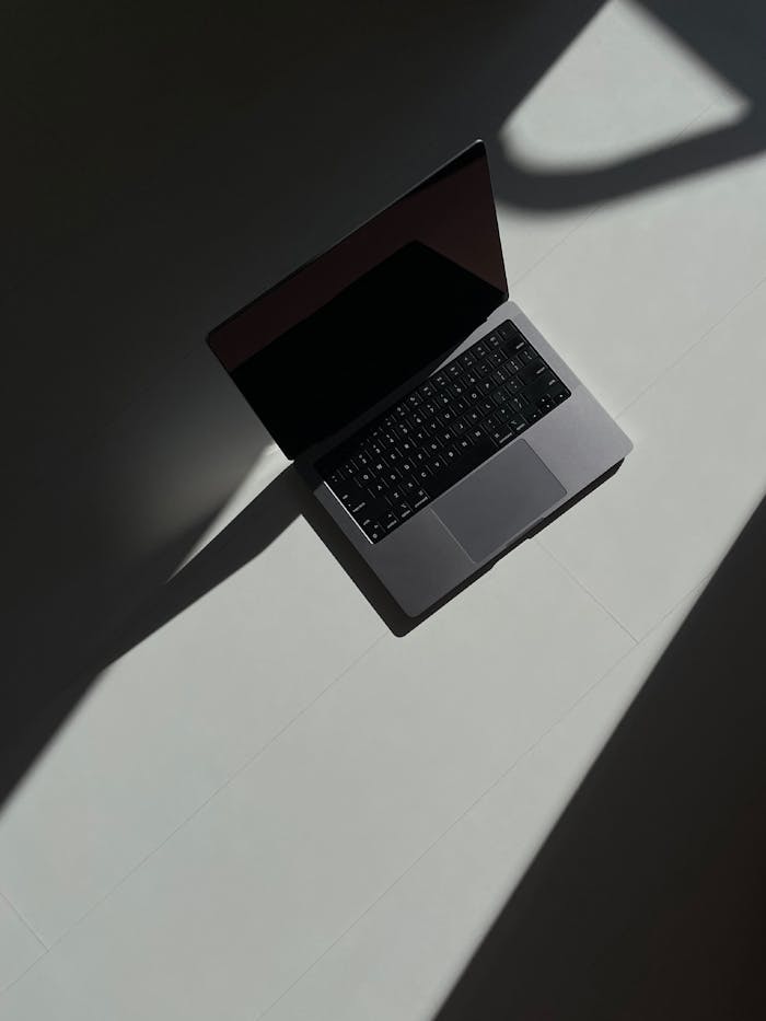 Artistic overhead view of an open laptop casting shadows on a flat surface.